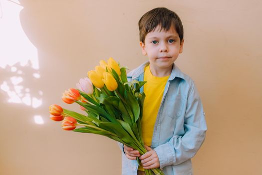A boy with a bouquet of tulips lifestyle . Postcard for March 8. Congratulations on Women's Day. Congratulations on Mother's Day. Flowers are tulips. Baby and flowers