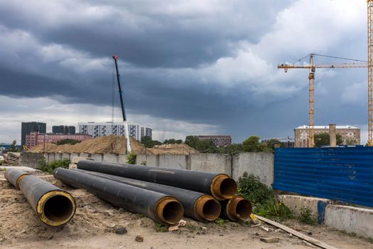 Moscow, Russia - 07 June 2021, Long factory pipes lie on the ground against the backdrop of a residential area under construction
