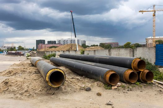 Moscow, Russia - 07 June 2021, Long factory pipes lie on the ground against the backdrop of a residential area under construction