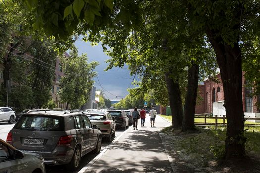 Moscow, Russia - 07 June 2021, People walk along the sidewalk. Sunlight in the skylight of the trees. Poplar fluff flies from the trees