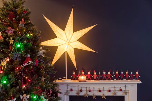 Red paper men holding hands on white and a large paper star on the background of tree there is an artificial fireplace on the background of a dark blue wall as an interior decoration for Christmas