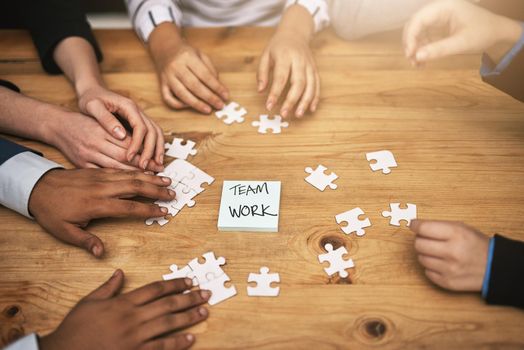 High angle shot of a group of unrecognizable coworkers building a puzzle on their boardroom table.