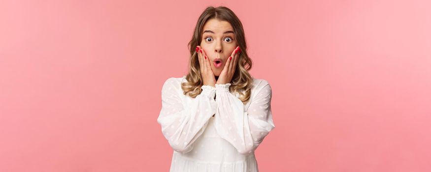 No way, what a story. Stunned and amazed blond girl listening to gossips with excitement and interest, hold hands on cheeks say wow and stare astonished camera, standing pink background.