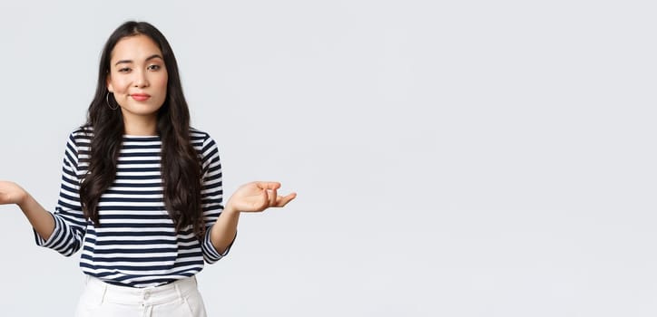 Lifestyle, beauty and fashion, people emotions concept. Clueless and unbothered asian woman shrugging with hands spread sideways and unaware smirk, standing white background.