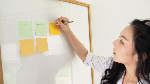 A woman using sticky postit and analysis data report during writing make note some data on notepad, Business financial concept.