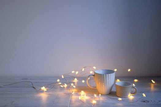 Minimalistic Scandinavian style. Two cups of coffee or tea of different sizes for two and garland on on the table. Empty space.