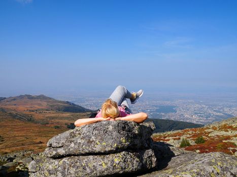 a woman lies on top of a mountain with her legs crossed and looks up at the sky.