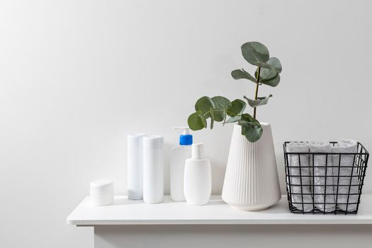 Bathroom interior. Metal basket with rolled face towels, white grooved vase with eucalyptus branch, shampoo and cream jars on the shelf in the spa salon