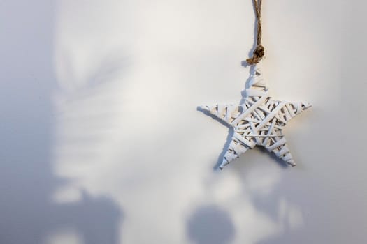 A white wicker willow star hangs on the wall. The shadow from the Christmas tree. Place for text. Copy space