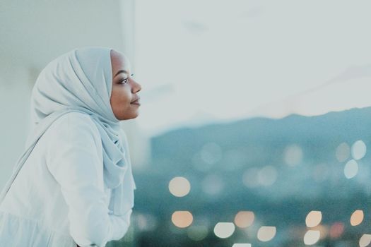 African Muslim woman in the night on a balcony smiling at the camera with city bokeh lights in the background. High-quality photo