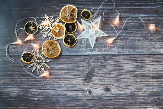 Dried orange slices, thread stars, cut snowflakes, garland on a wooden table. Place for your text. Shooting from above. Copy space