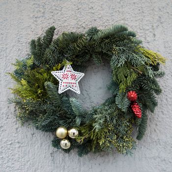 Christmas wreath of fir branches with decorations, star, balls hanging on the grey wall of the house