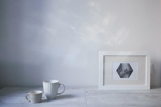 Scandinavian style. Interior Design. A white cup of different size, a frame for a photo are on the table. Empty space for text