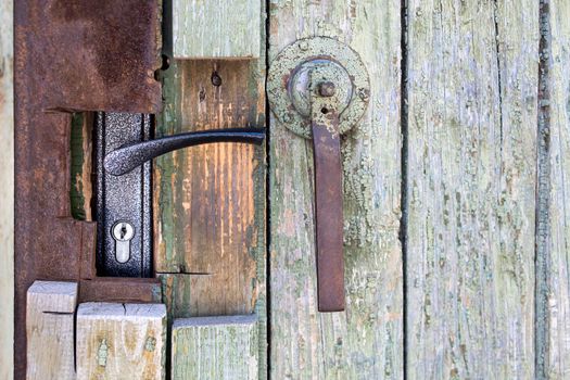Fragment of an old green wooden door with a handle and a lock with peeling paint