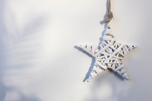 A white wicker willow star hangs on the wall. The shadow from the Christmas tree. Place for text. Copy space
