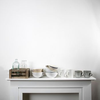 kitchen utensils, cups of different sizes and shades, bowls, bottles, storage items, are on a white dresser. Square frame