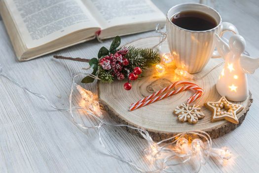 A cup of coffee on a wooden stand, a gingerbread cookie tied with a rope, a garland on the table. Artificial spruce branch with red berries. Breakfast at Christmas. Scandinavian style. Copy space