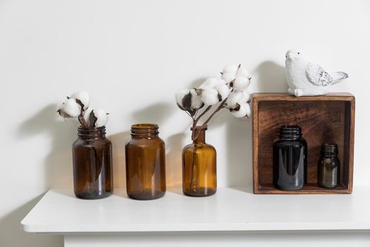 A row of brown small pharmacy bottles instead of vases with branches of blossoming cotton and wooden boxes on a white surface of the fireplace as an interior decoration