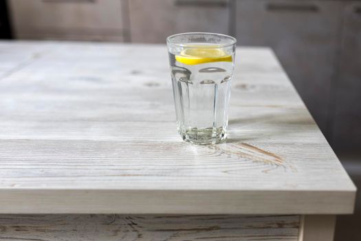 Transparent glass tables with a slice of lemon is on a wooden table in a beige kitchen interior. Empty space