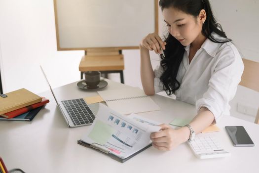 Young asian entrepreneur cogitating thinking making important decision at workplace. Concentrated serious office worker millennial woman analysing results.