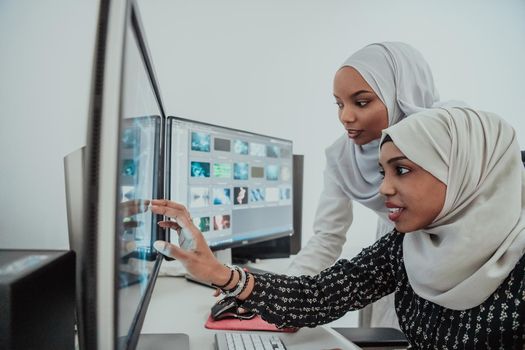 Friends at the office are two young Afro-American modern Muslim businesswomen wearing scarfs in a creative bright office workplace with a big screen. High-quality photo