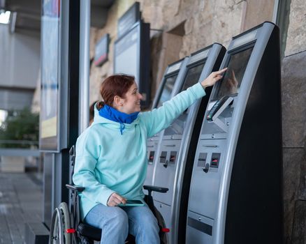 Caucasian woman in a wheelchair buys a train ticket at a self-service checkout