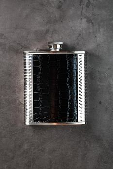 Pocket flask made of steel in leather finish with an alcoholic drink on a dark background with copy space