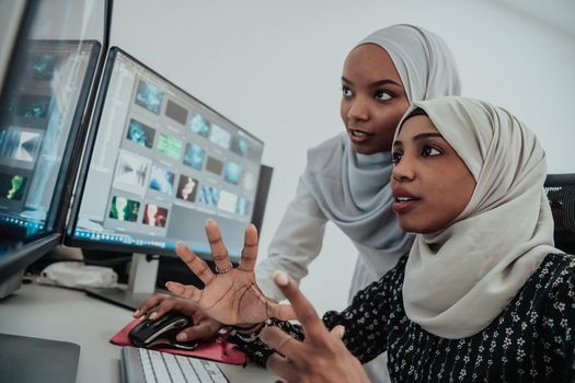 Friends at the office are two young Afro-American modern Muslim businesswomen wearing scarfs in a creative bright office workplace with a big screen. High-quality photo