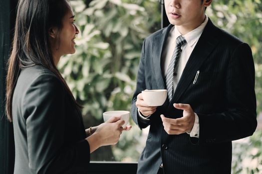 Coffee break. Group business people, standing in modern office, holding a cups, smiling standing at the window.