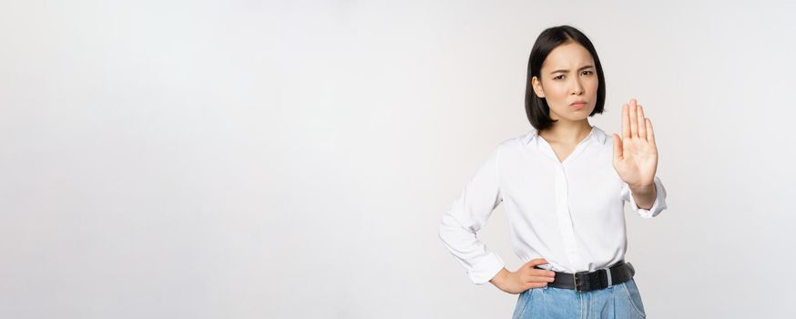 Portrait of young woman extending one hand, stop taboo sign, rejecting, declining something, standing over white background. Copy space