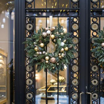 Christmas wreath of fir branches with decorations hanging on a transparent door with metal inserts