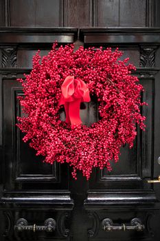 A red wreath collected from hawthorn berries and branches hangs on the black door. Christmas decoration