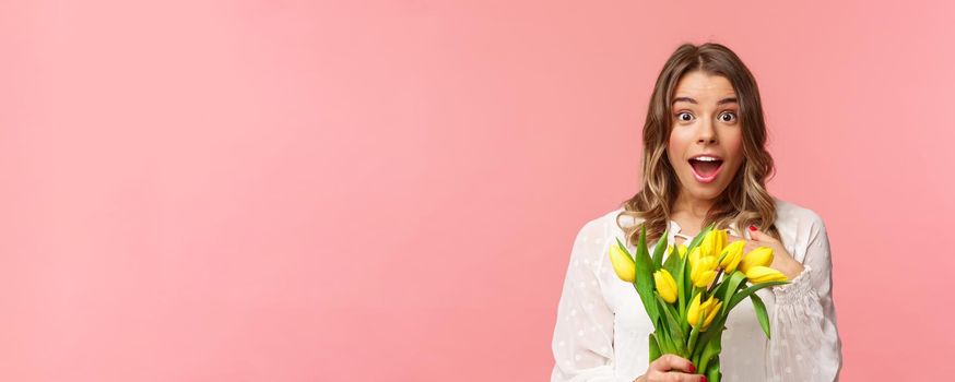 Spring, happiness and celebration concept. Close-up of surprised and wondered young blond girl in white dress, receive yellow tulips and pointing herself with disbelied and amazement, didnt expact.