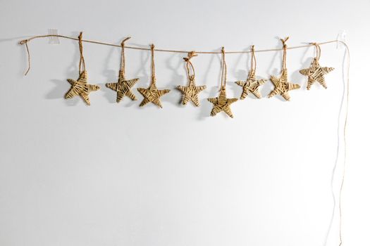 A handmade garland of braided stars is on a white wall. Place for text. Copy space