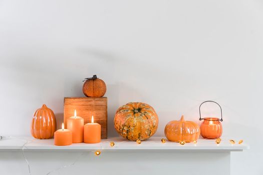 Porcelain and natural pumpkins, orange candles on a white table, Halloween decorations.