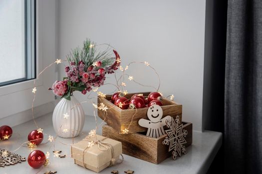 An artificial spruce branch, decorated with ivy leaves, apples and hawthorn berries. Lighted candles in wooden box, red glass balls, winter composition decorates interior on eve of Christmas
