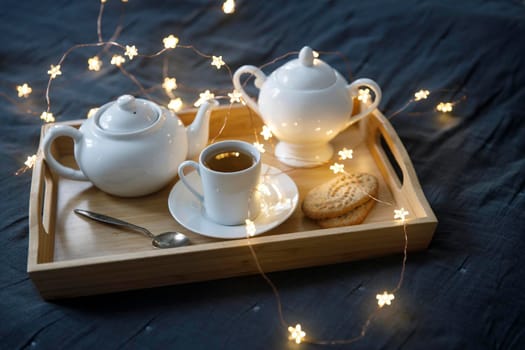 Interior and home cosiness concept. Top view, A cup of tea, a sugar bowl, a spoon, a teapot, a garland on a tray on the bed. Breakfast.