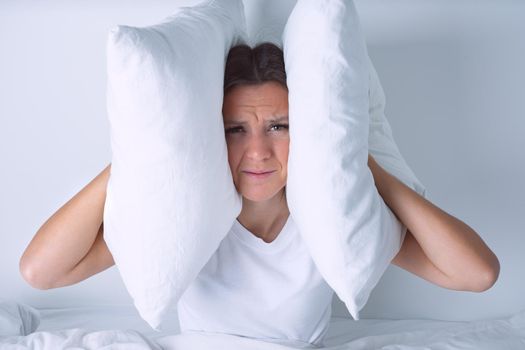 Young woman disturbed by noisy neighbours. Woman struggling from noise in bed and covering ears with pillows. High quality photo