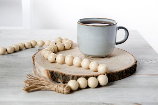 blue ceramic cup on a wooden round cut, beads, a rosary for prayer on a beige table against a white wall. Place for text