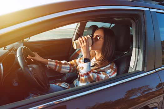 Young beautiful stylish woman driving her new car and drinking coffee on a sunny day. Concept for car rental. High quality photo