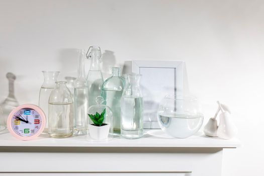 A set of water bottles of different shapes with a photo frame and a pot with artificial succulent is on the dresser. Copy space