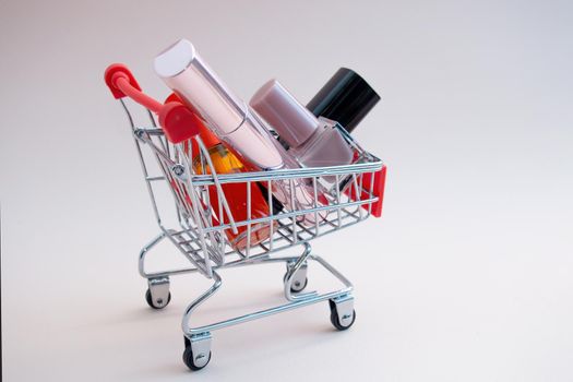 Front view of a shopping cart with makeup products on a pink background. Cosmetic shopping concept. photo