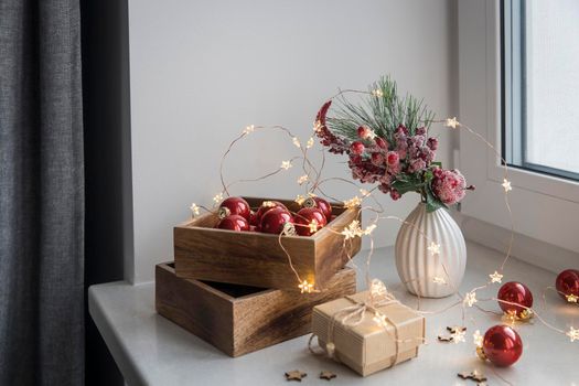 An artificial spruce branch, decorated with ivy leaves, apples and hawthorn berries. Lighted candles in wooden box, red glass balls, winter composition decorates interior on eve of Christmas