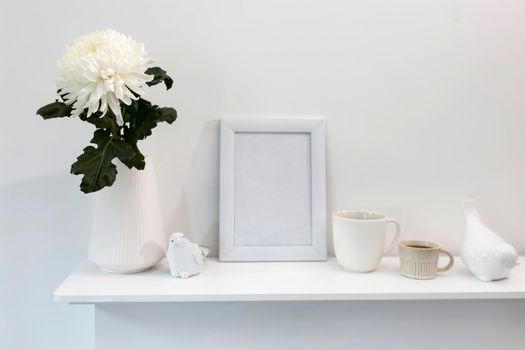 Large chrysanthemum in a glass vase. Photo frame with place for text, two corrugated cups with coffee and ceramic figurines of birds on the table. Office decoration. Copy space