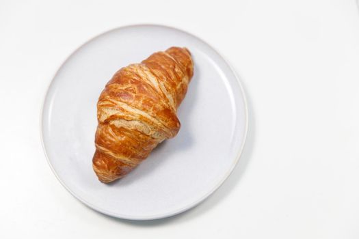 Freshly baked croissant on gray round plate on white background