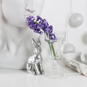 Ceramic figurines of Easter bunnies of different sizes on the table. Blue and white hyacinths in glass cups on a white background. Easter design