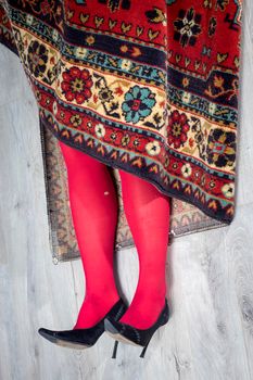Red female legs in torn tights stick out of the carpet