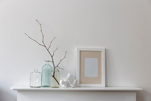 Scandinavian style. A bottle of water with a branch, two empty bottles of different shapes, figurines of birds are on a white fireplace. Copy space