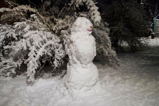 Snowman on is the playground in the snowfall at night
