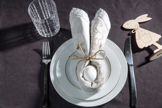 Napkin folder idea. Easter table. Easter holiday table setting with egg in grey napkin Easter Bunny on a brown linen background. Copy space, top view, flat lay.